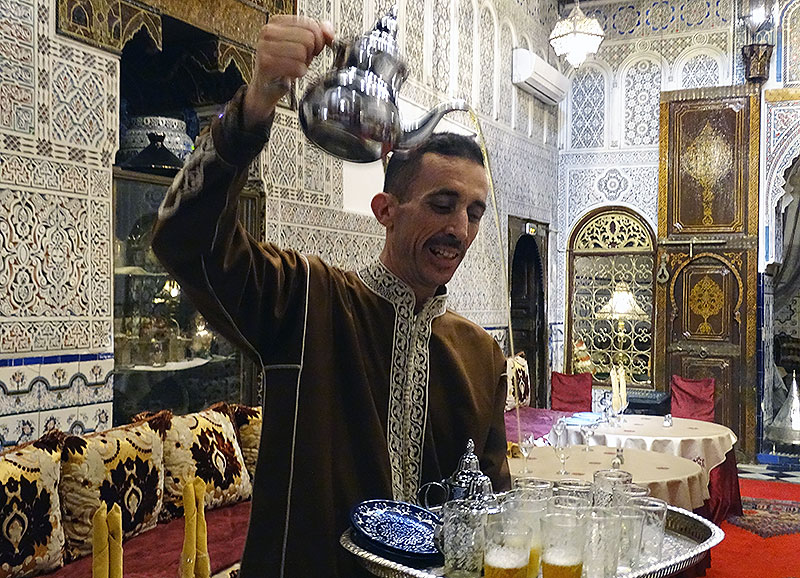 Kellner in Marrakesch schüttet Tee in kleine Gläser