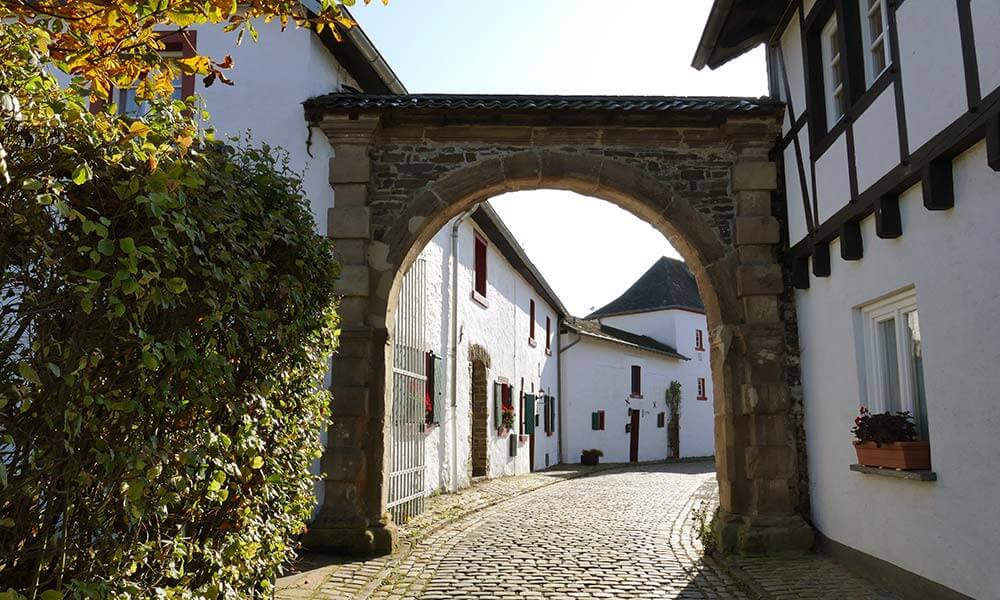 In Reifferscheid: Straße mit Kopfsteinpflaster und weißen Häusern hinter einem Tor