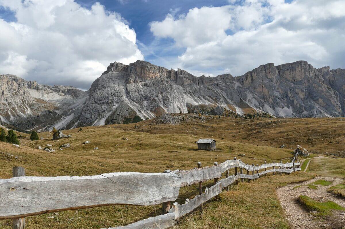 Weg an einem Zaun entlang, im Hintergrund Berge