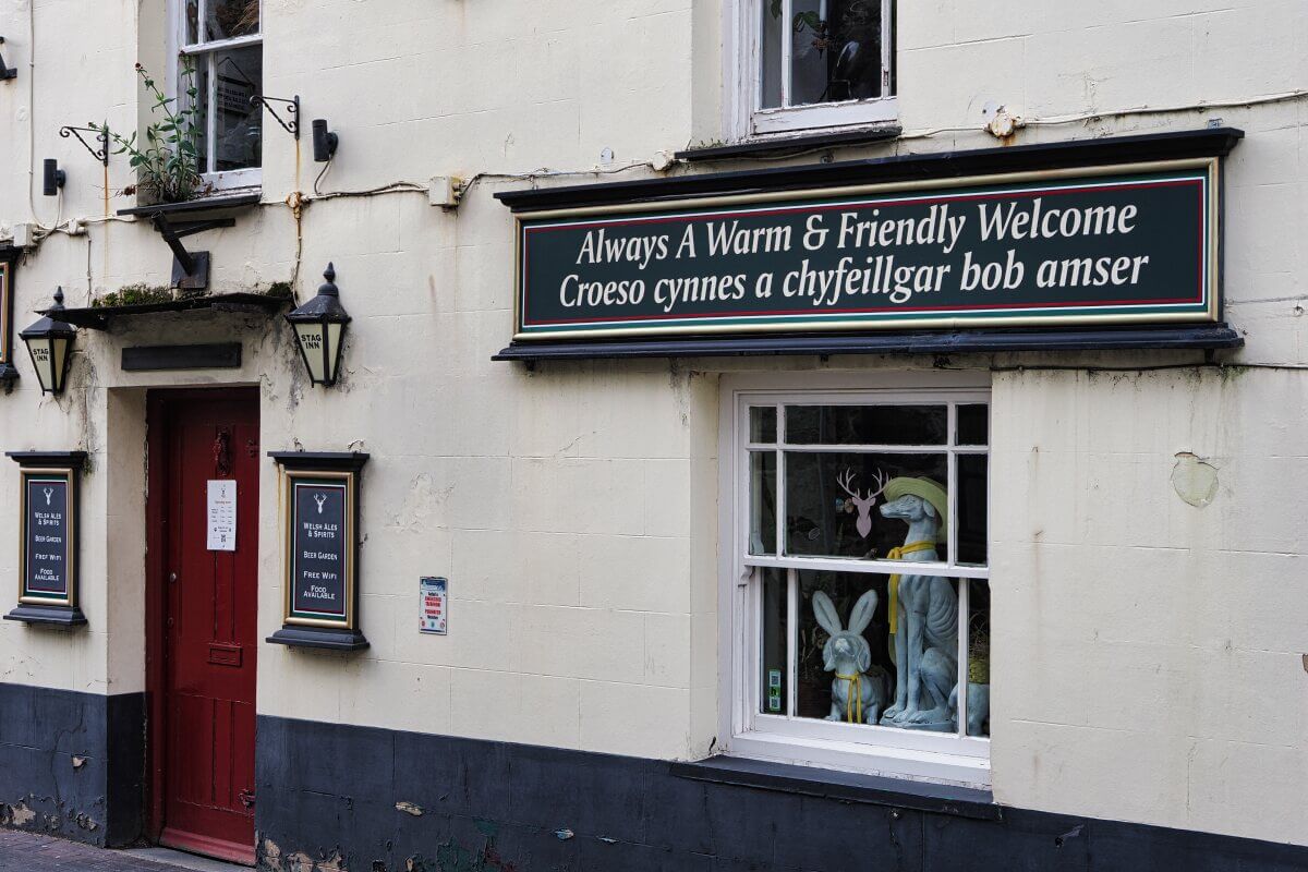 Ein weißes Haus mit roter Tür und einem Schild mit der Aufschrift „Always A Warm & Friendly Welcome“ auf Englisch und Walisisch.