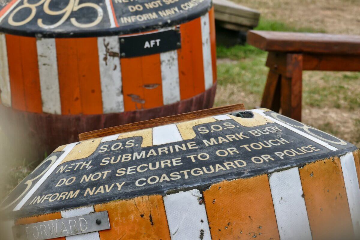 Nahaufnahme einer orange-weiß gestreiften Boje mit dem Schild „S.O.S. U-Boot-Markierungsboje. Nicht befestigen oder berühren. Informieren Sie die Küstenwache oder die Polizei." 