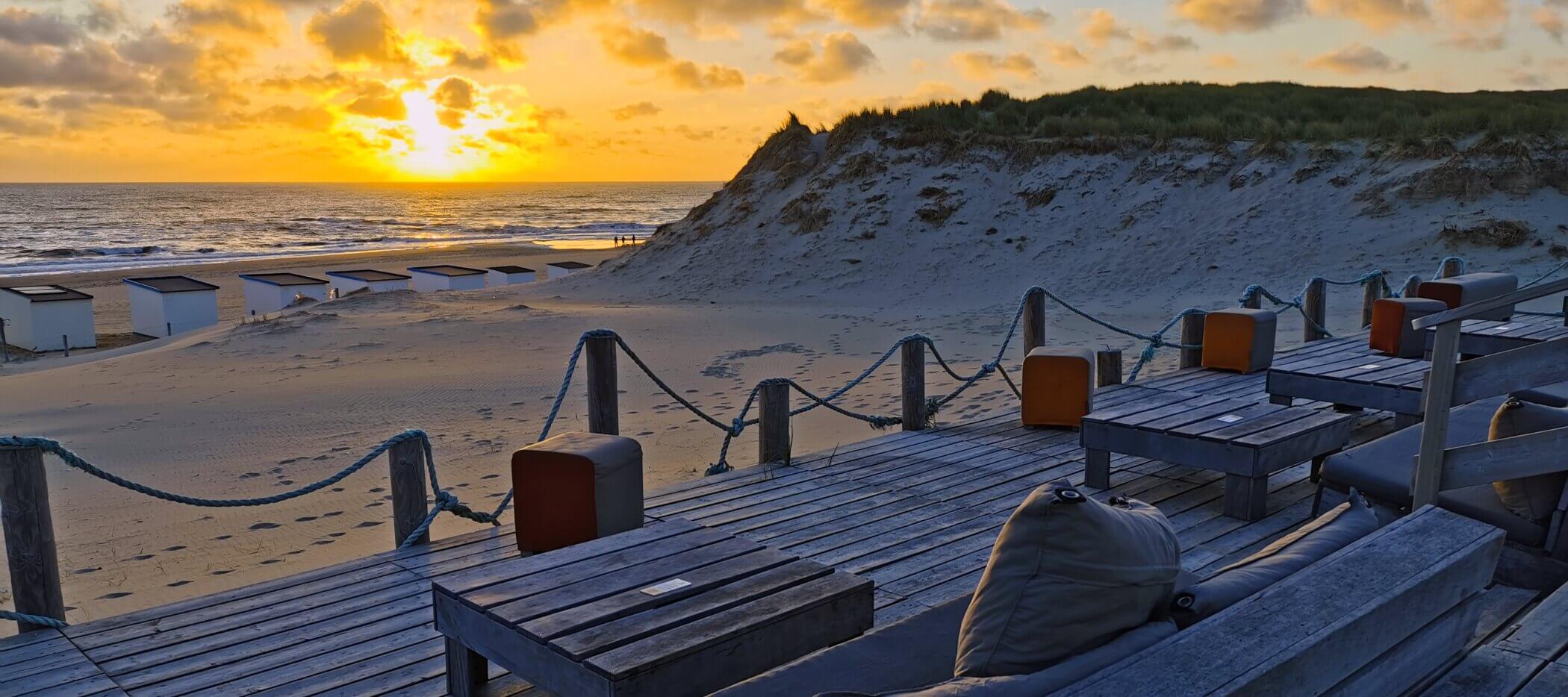 sonnenuntergang-texel Sonnenuntergang am Strand, im Vordergrund eine hölzerne Terrasse mit Sitzgelegenheiten.