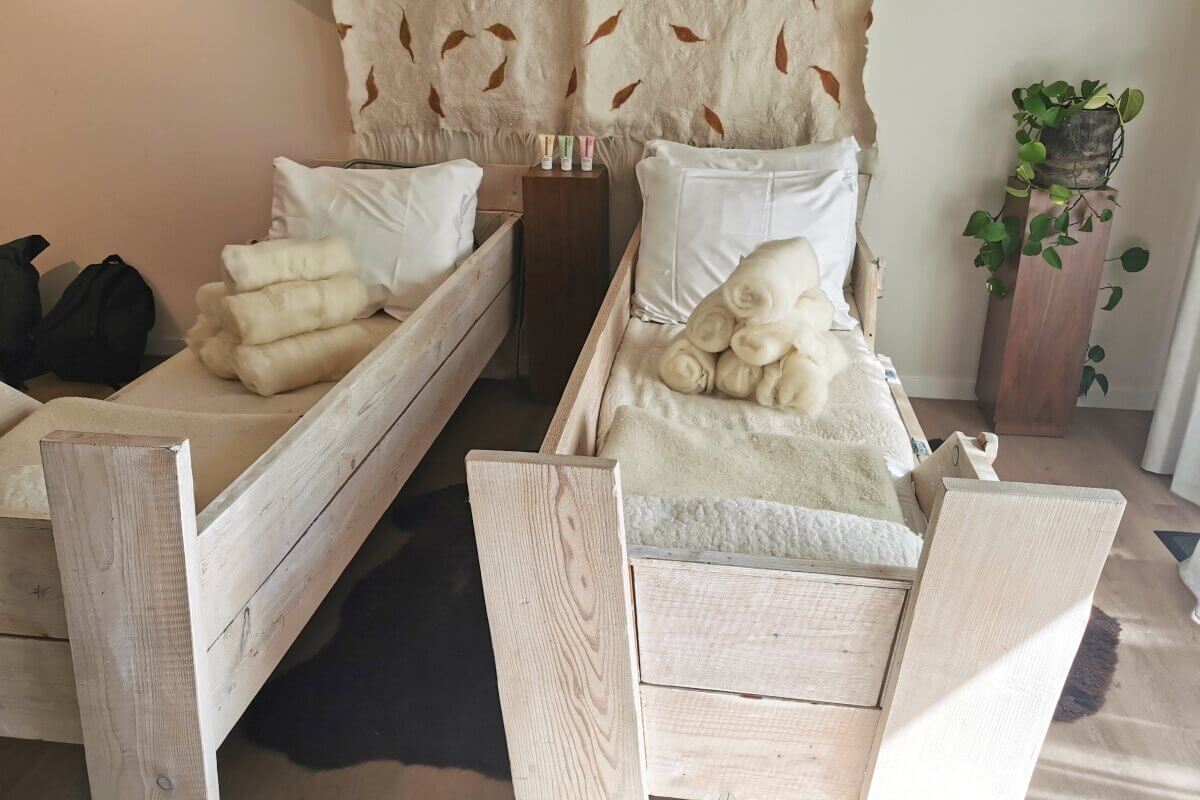 Zwei rustikale Holzbetten mit weißer Bettwäsche und gerollter Schafswolle in einem gemütlichen Zimmer mit einer Pflanze.