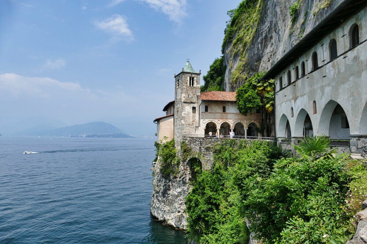 Historisches Steinkloster, das in einen Felsen gebaut wurde und den Lago Maggoire mit Bergen im Hintergrund überblickt. 