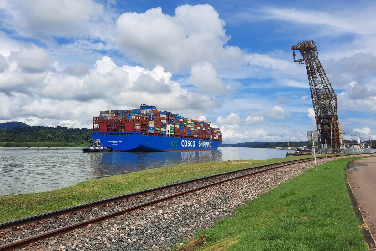 Großes Frachtschiff mit vielen Containern fährt im Kanal an einem Kran vorbei