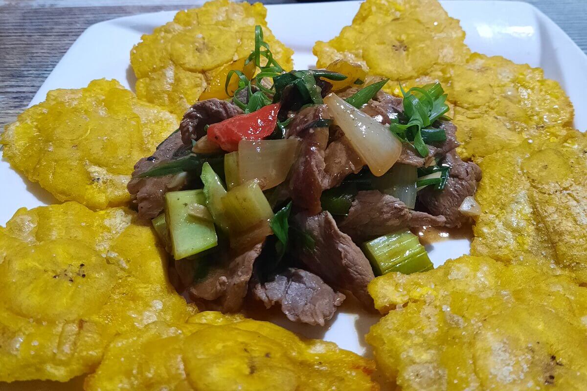 Ein Teller mit gebratenen Kochbananen, die um gebratenes Rindfleisch mit Gemüse auf einem weißen Teller angeordnet sind.