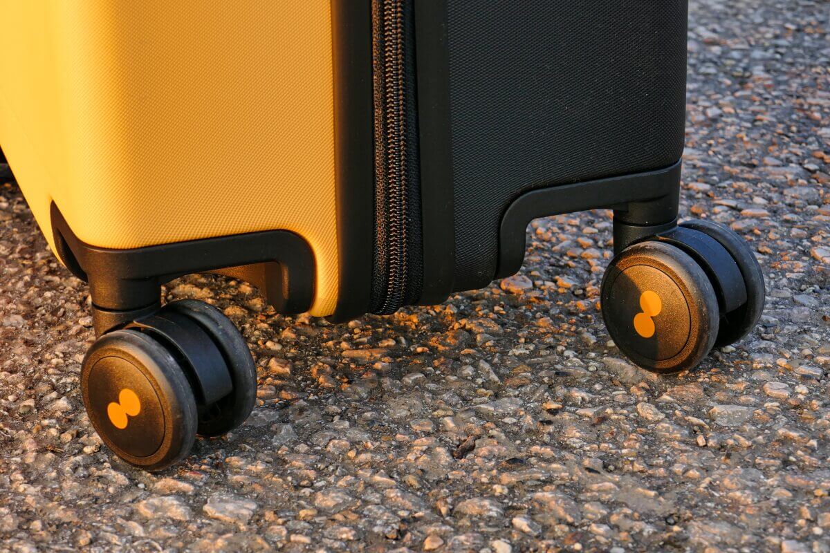 Nahaufnahme eines gelb-schwarzen Koffers mit Rädern auf strukturiertem Pflaster.