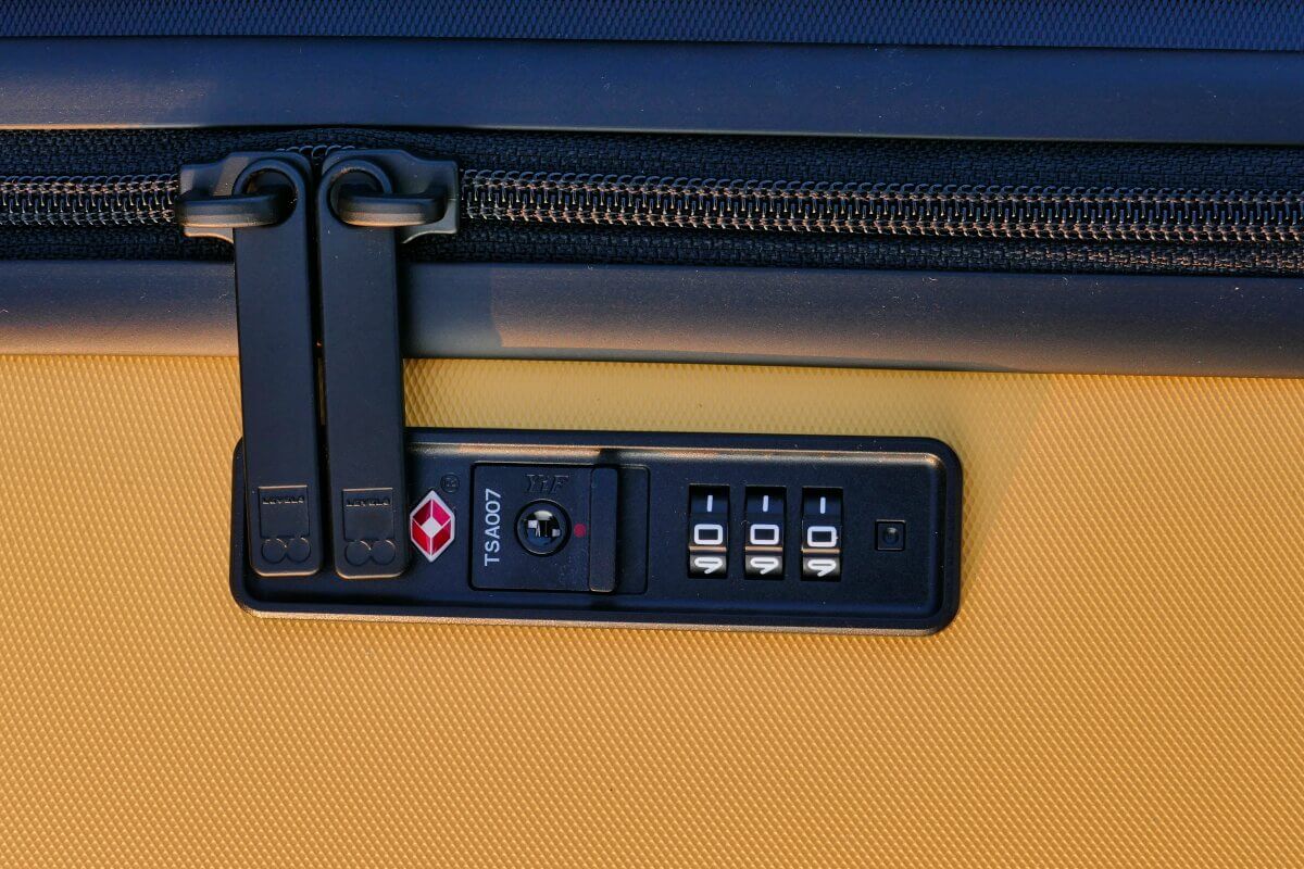 Nahaufnahme eines gelben Koffers mit einem schwarzen TSA-Zahlenschloss und Reißverschlüssen.