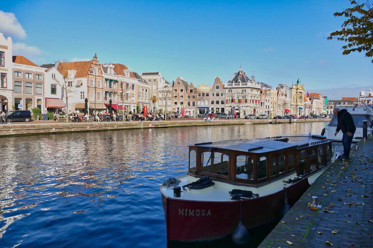 Ein Kanalboot mit der Aufschrift Mimosa, das an einem sonnigen Tag in Haarlem an bunten Gebäuden anlegt.