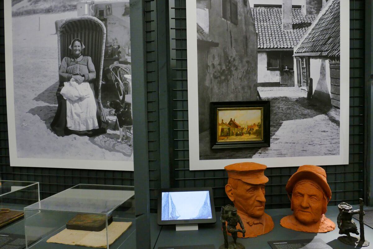 Museumsausstellung mit alten Fotos, Tonbüsten eines Mannes und einer Frau sowie verschiedenen kleinen Kunstwerken und Artefakten.