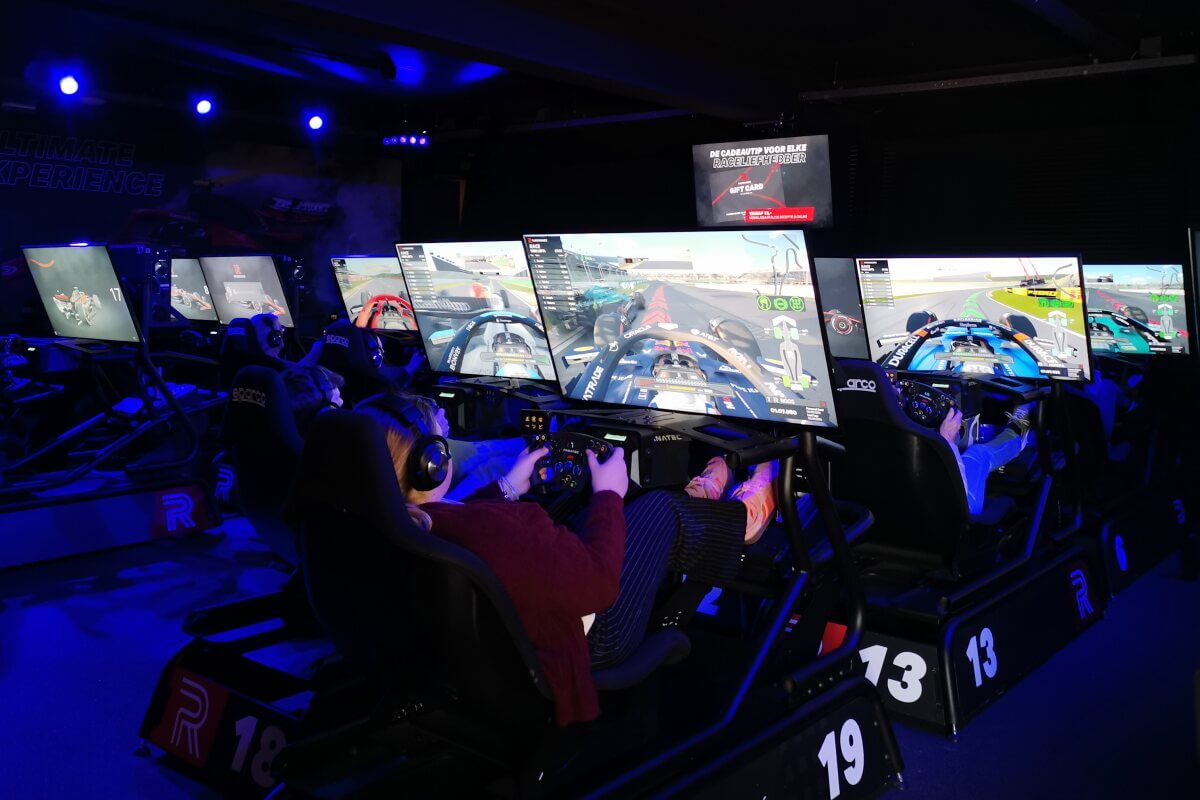 Menschen mit Rennsimulatoren in einem dunklen Raum, jeder konzentriert sich auf seinen eigenen Bildschirm, auf dem ein Autorennspiel angezeigt wird.