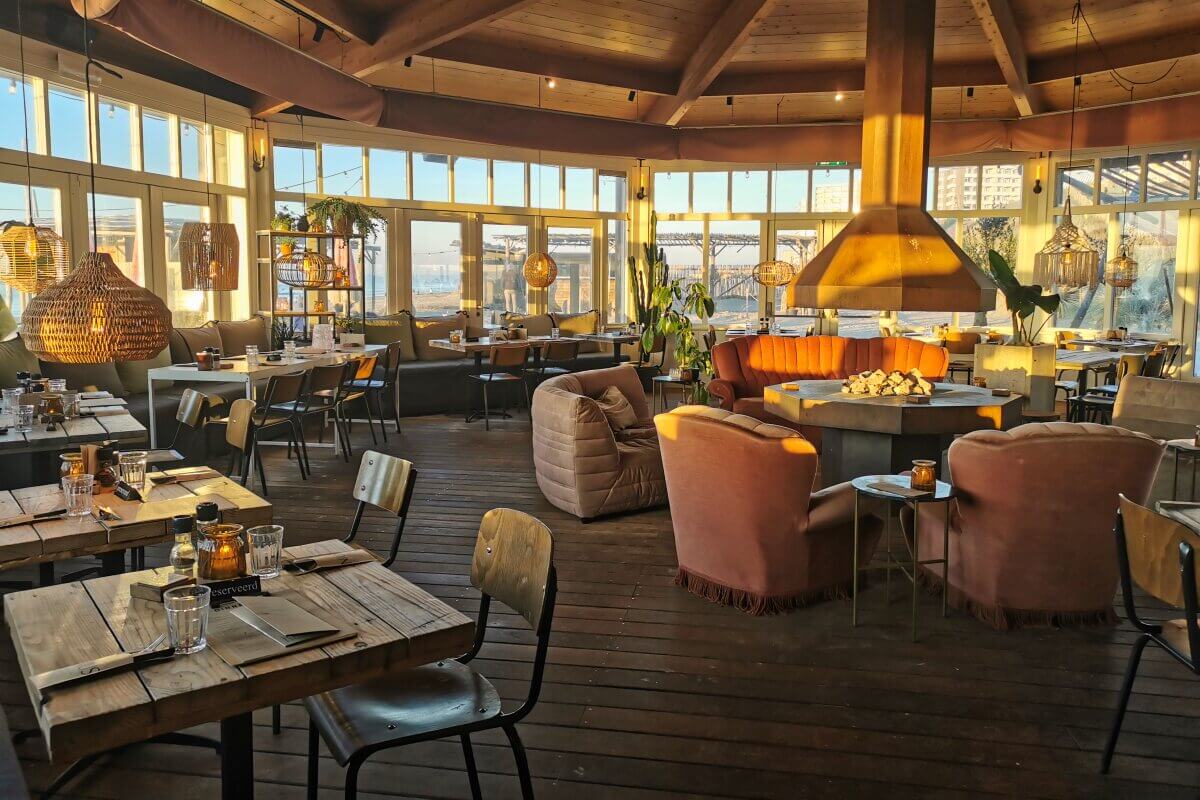 Gemütliches Restaurant mit Holztischen, sanfter Beleuchtung und großen Fenstern, die warmes Sonnenlicht hereinlassen.