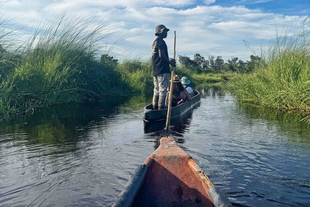 Ein Mann im Holzkanu paddelt Gäste durch grasbewachsene Feuchtgebiete unter einem blauen Himmel mit vereinzelten Wolken.