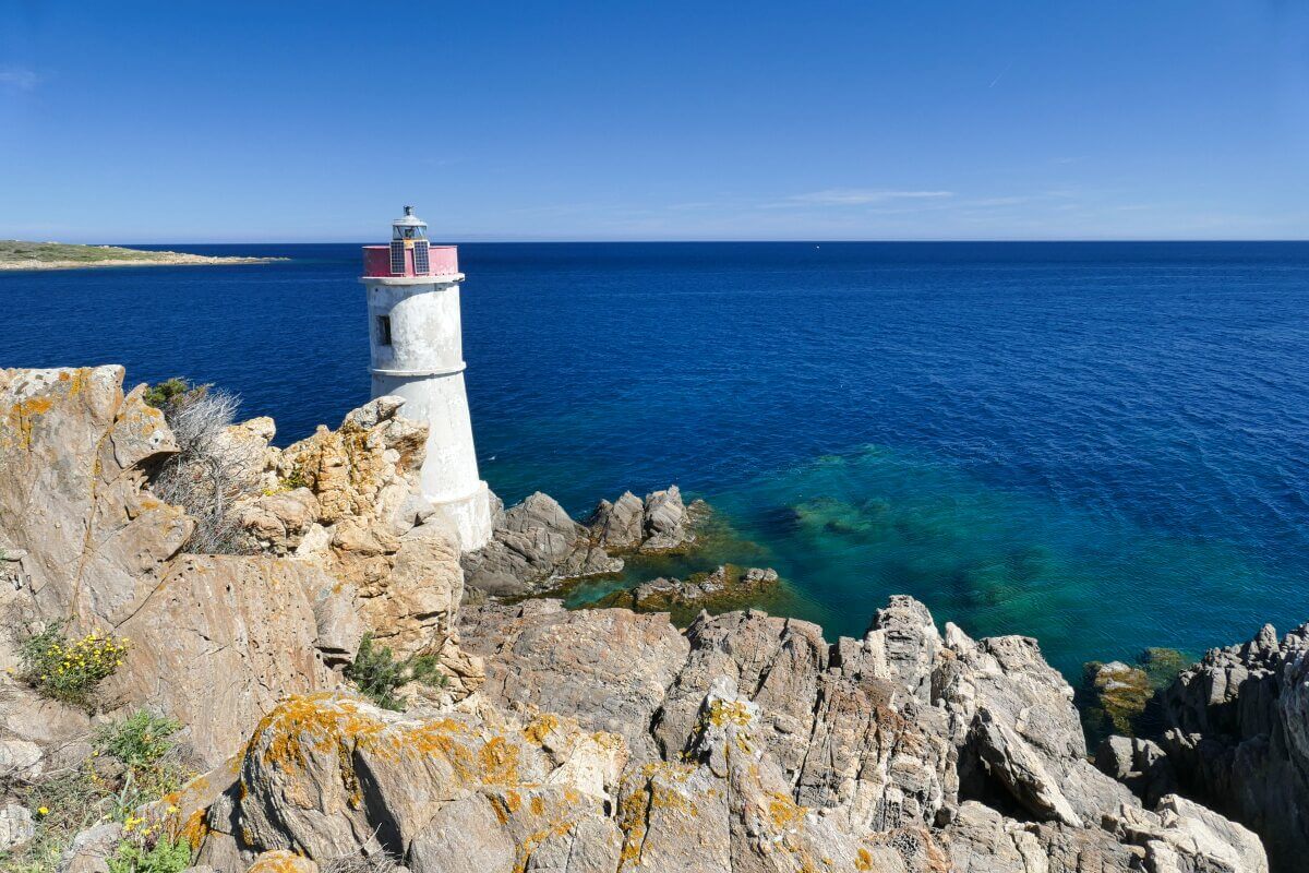 Ein weißer Leuchtturm auf felsigen Klippen überblickt ein klares blaues Meer unter einem strahlenden, sonnigen Himmel.