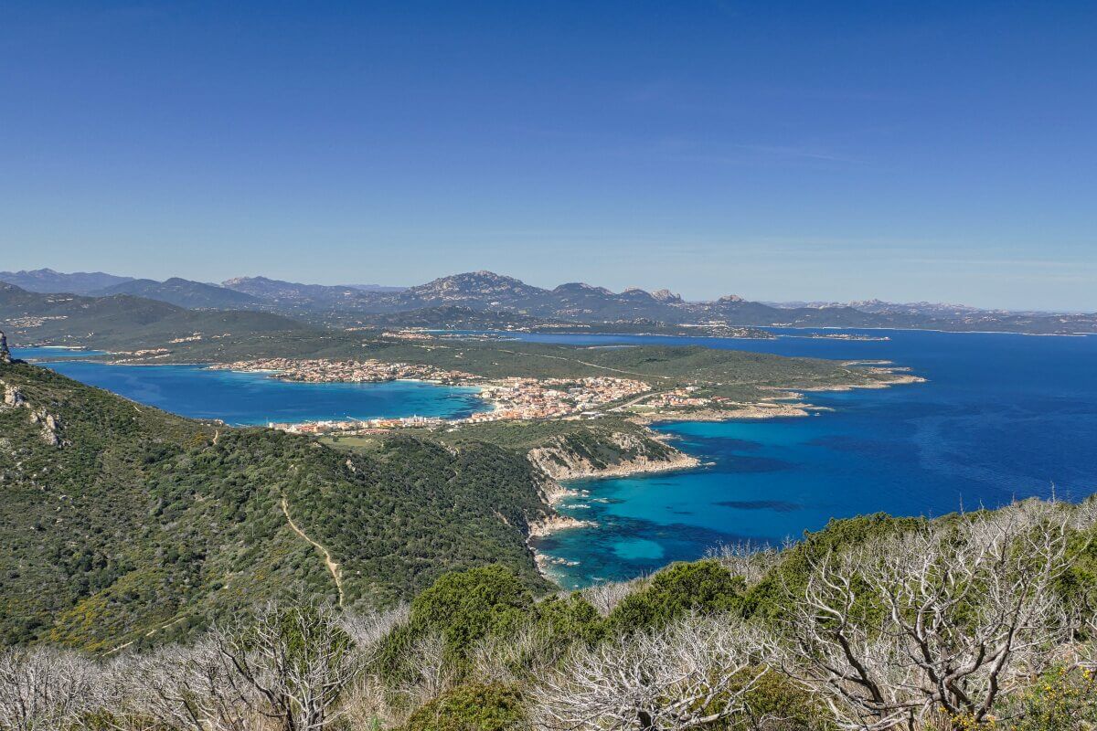 Eine Küstenstadt mit blauen Buchten, grünen Hügeln und Bergen unter einem strahlend blauen Himmel.