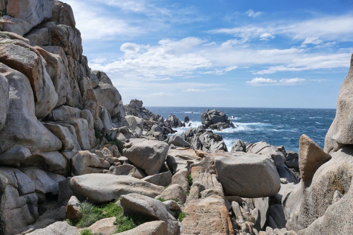 Große Granitfelsen am Meer, wo die Wellen unter einem teilweise bewölkten blauen Himmel brechen.
