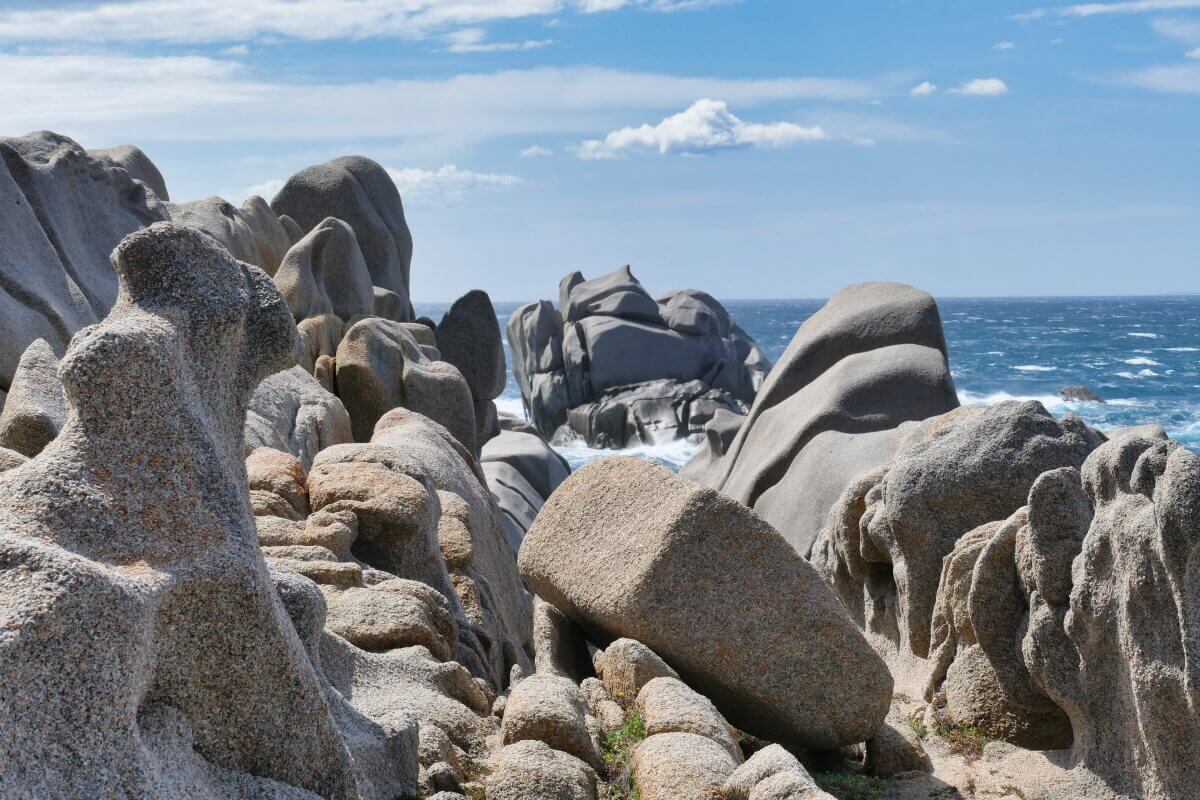 Zerklüftete Granitfelsen am Meer mit Wellen und einem teilweise bewölkten blauen Himmel im Hintergrund.