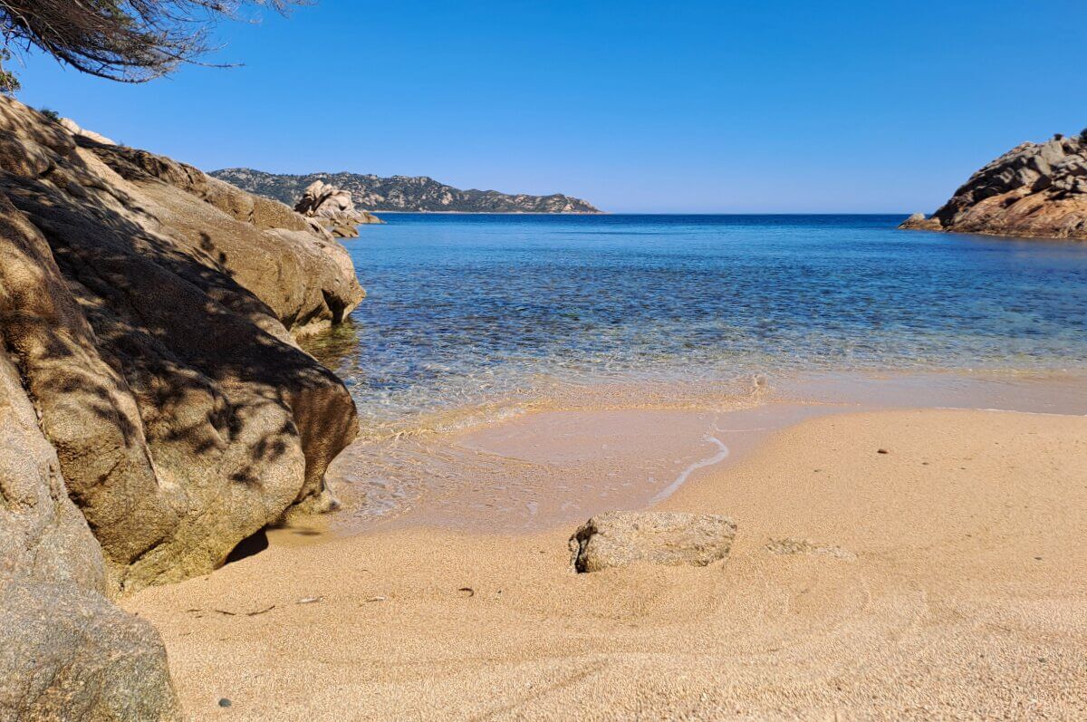 Klares blaues Meer, Sandstrand und felsige Küste unter einem strahlend blauen Himmel an einem sonnigen Tag.