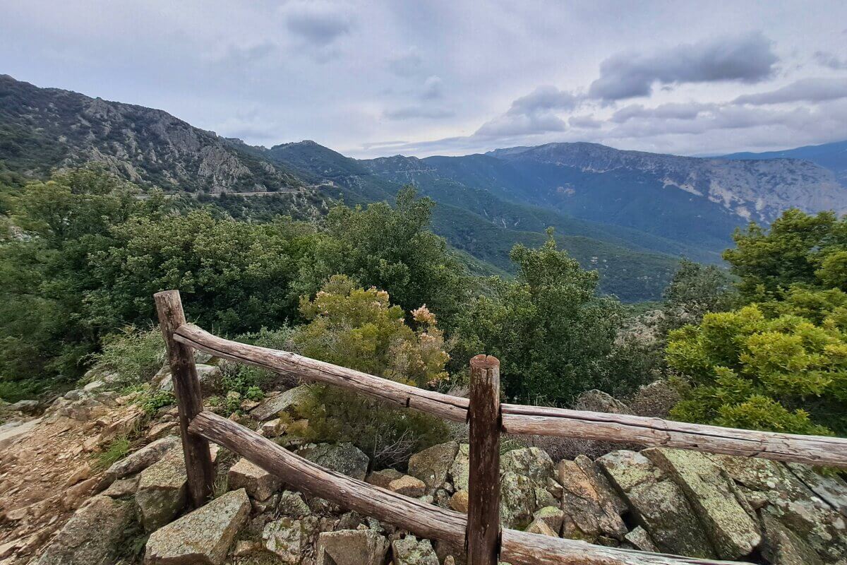Holzzaun mit Blick auf üppig grüne Berge und Täler unter einem bewölkten Himmel.