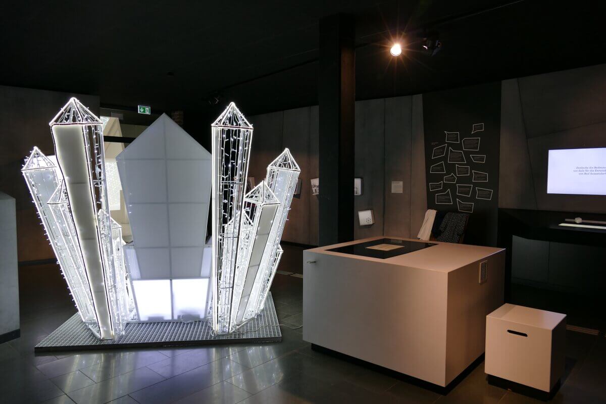 Eine moderne Museumsausstellung mit geometrischen, beleuchteten, kristallartigen Strukturen und einem eleganten, dunklen Interieur.